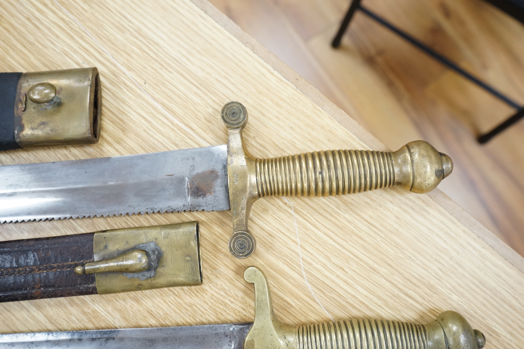 Three Continental infantry officer’s sidearms briquette, the first stamped Paris, in its brass mounted leather scabbard, another similar with sawback blade (illegible stamp), and another similar with thin blade, stamped